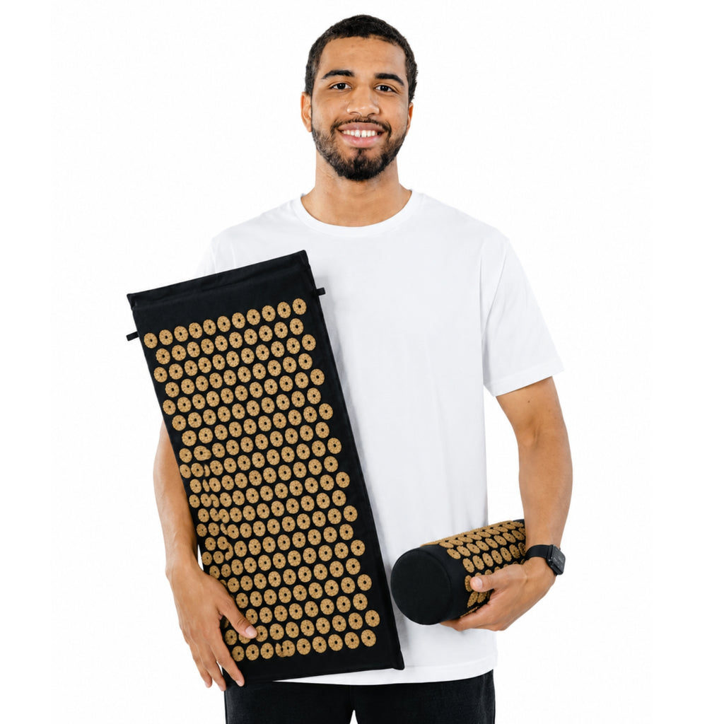 Personne tenant un tapis d’acupression noir et son coussin cervical sur fond blanc.