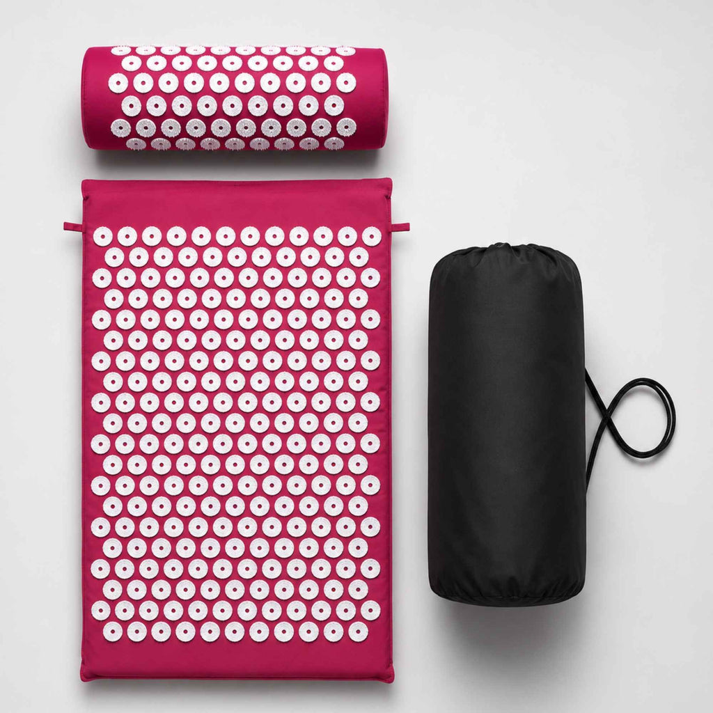 Kit de tapis d’acupression rose avec coussin cervical et sac de transport sur fond blanc.