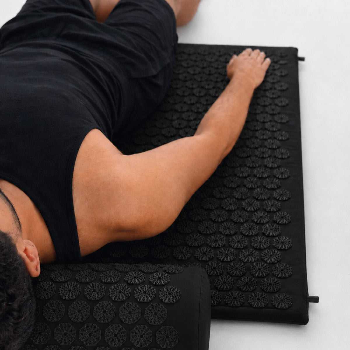 Personne allongée sur un tapis d’acupression noir pour favoriser la détente musculaire et le relâchement des tensions.